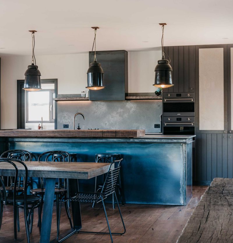 Contemporary kitchen and dining area in a Snowy Mountains home with dark cabinetry, timber floors and industrial pendant lights